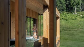A wooden cabin with a glass balcony overlooking a grassy area.