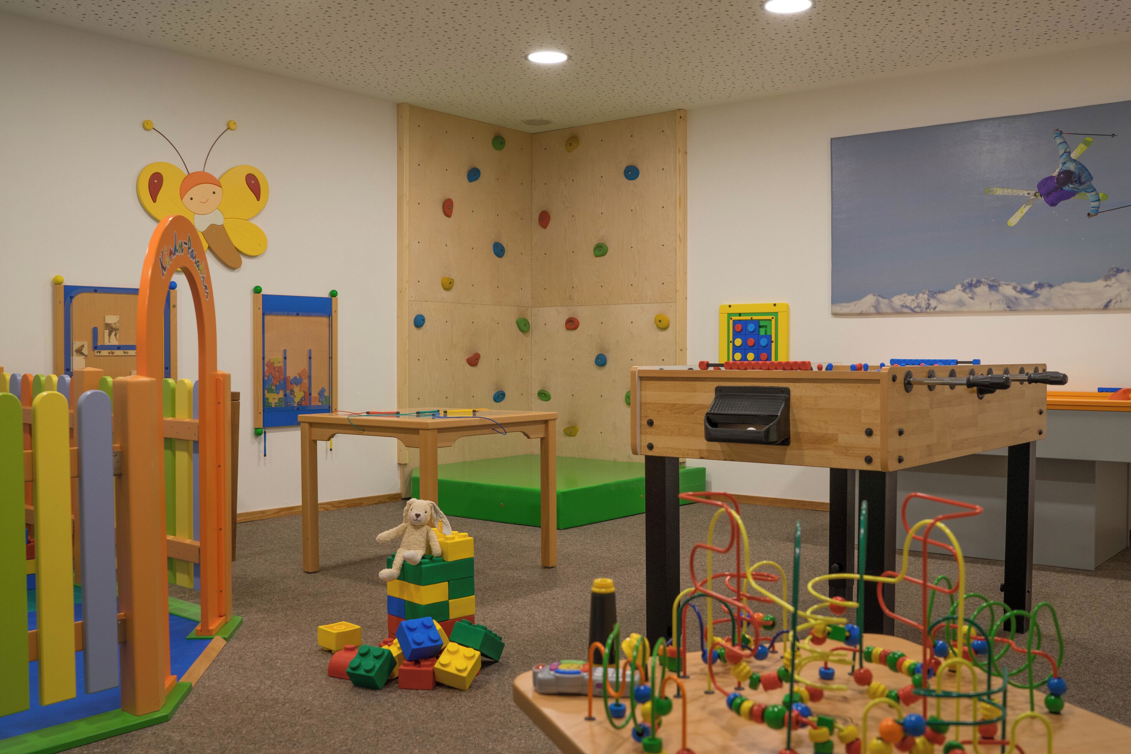Ein Spielzimmer mit Kletterwänden, einem Tischfußballtisch und verschiedenen Spielsachen.