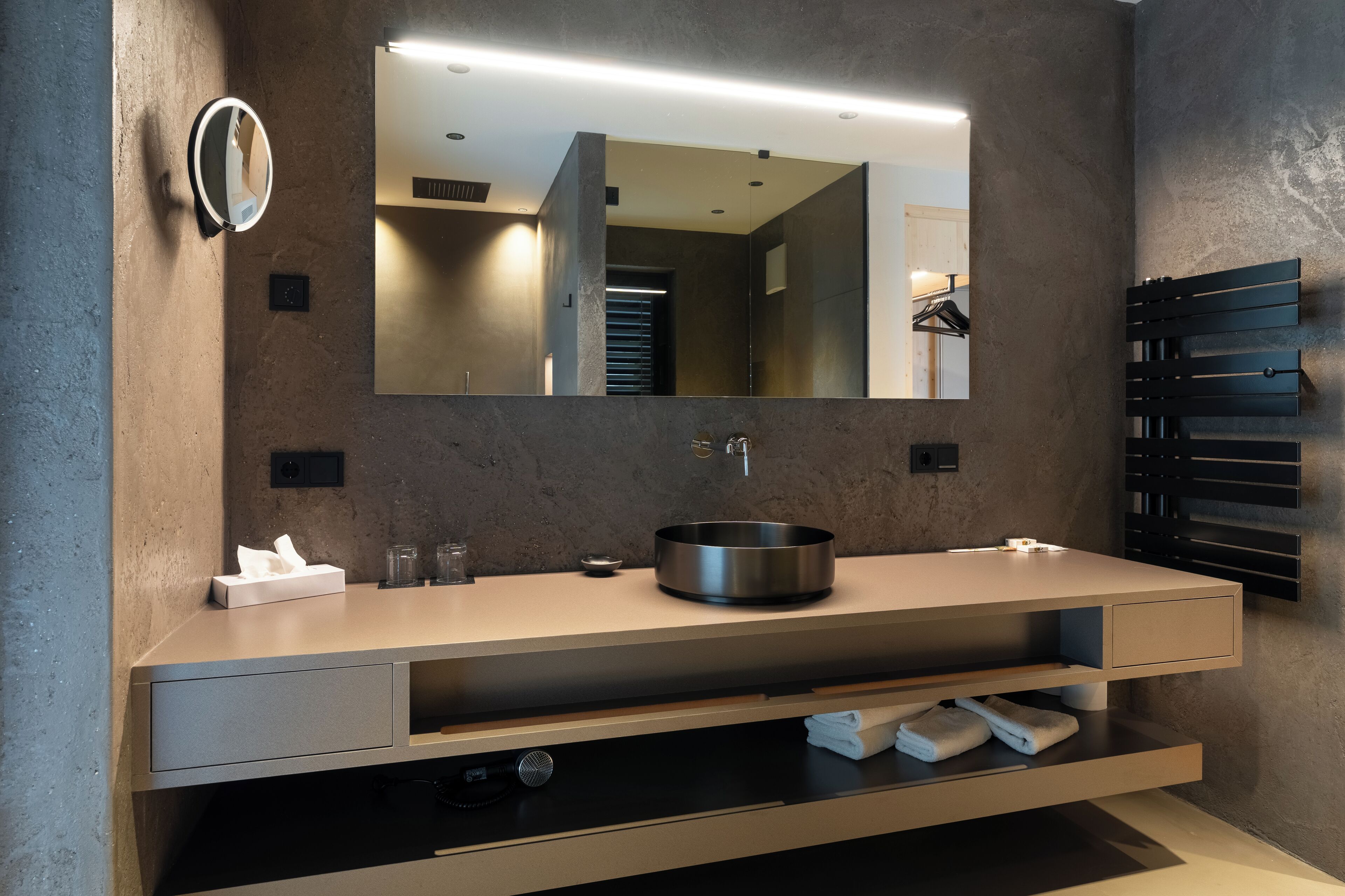 A modern bathroom with a large mirror, a round sink, and a towel rack.
