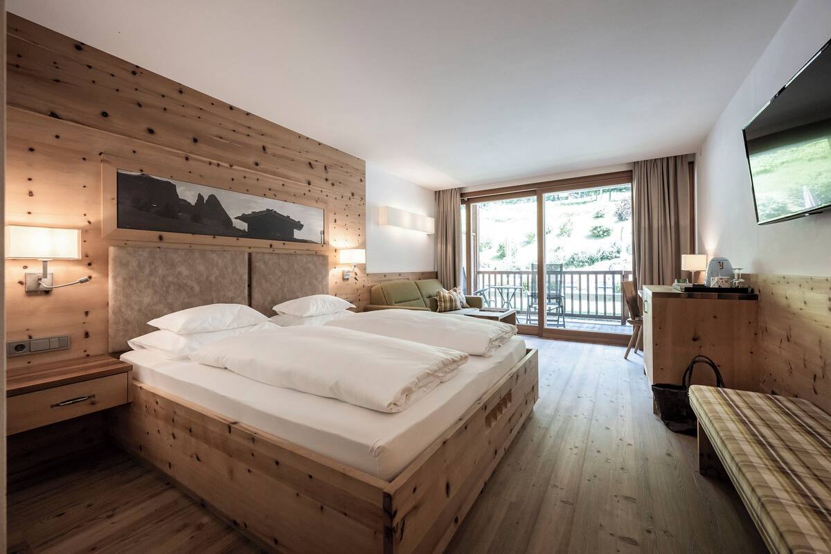 A hotel room with a wooden bed, a sofa, a TV, and a balcony with a view.