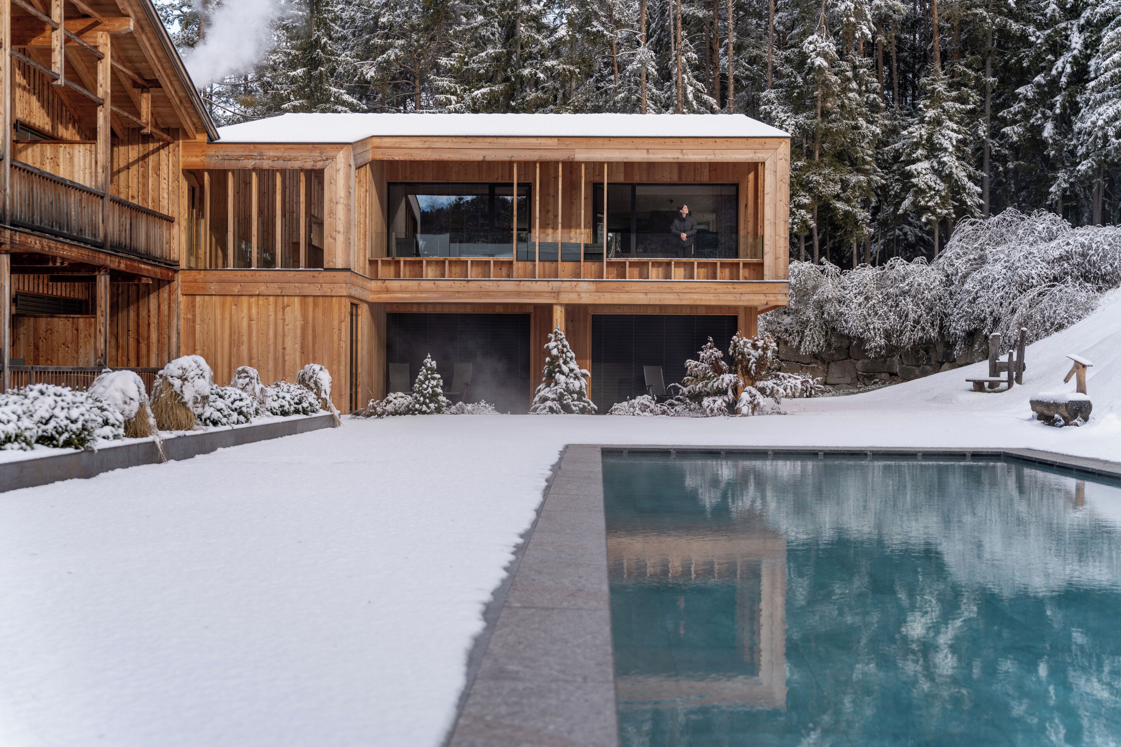 A wooden cabin with a pool, surrounded by snow-covered trees.