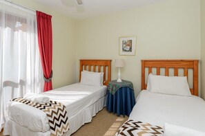 A hotel room with two single beds, a small table with a lamp, a picture on the wall, and a window with curtains.