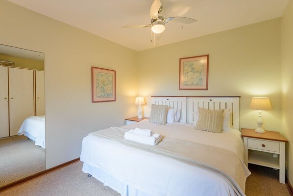 A neatly arranged bedroom with a bed, bedside tables, a ceiling fan, and framed artwork on the walls.