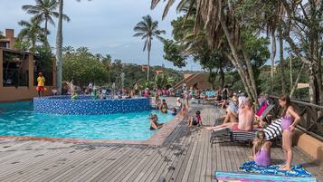 A pool area with a wooden deck, lounge chairs, and palm trees.