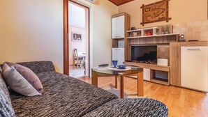 Una sala de estar acogedora con un sofá, una mesita y un televisor. Hay una zona de cocina con estufa, refrigerador y un armario de madera.