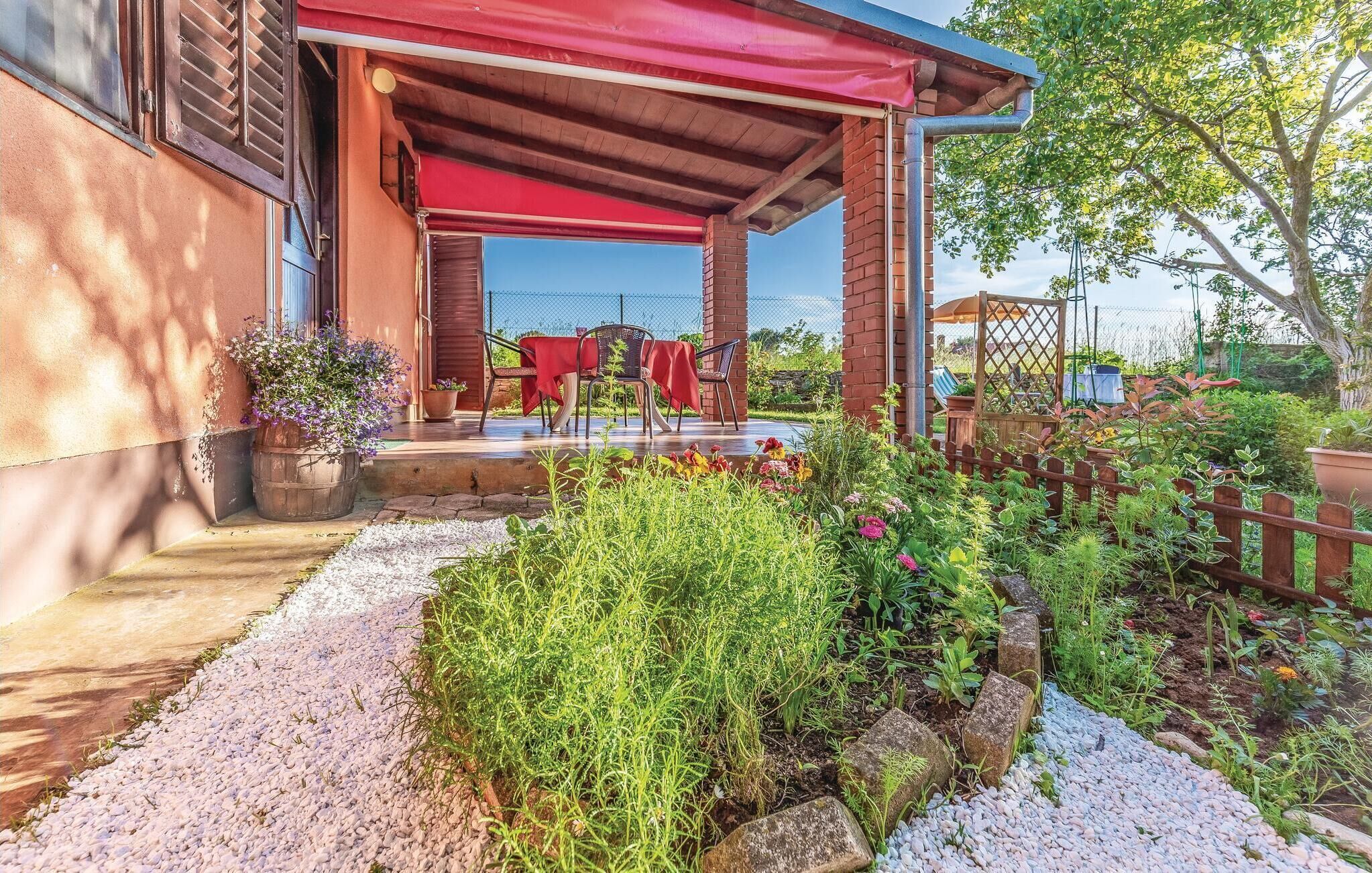 An outdoor patio with a red canopy, a brick wall, and a garden area with various plants and a wooden fence.