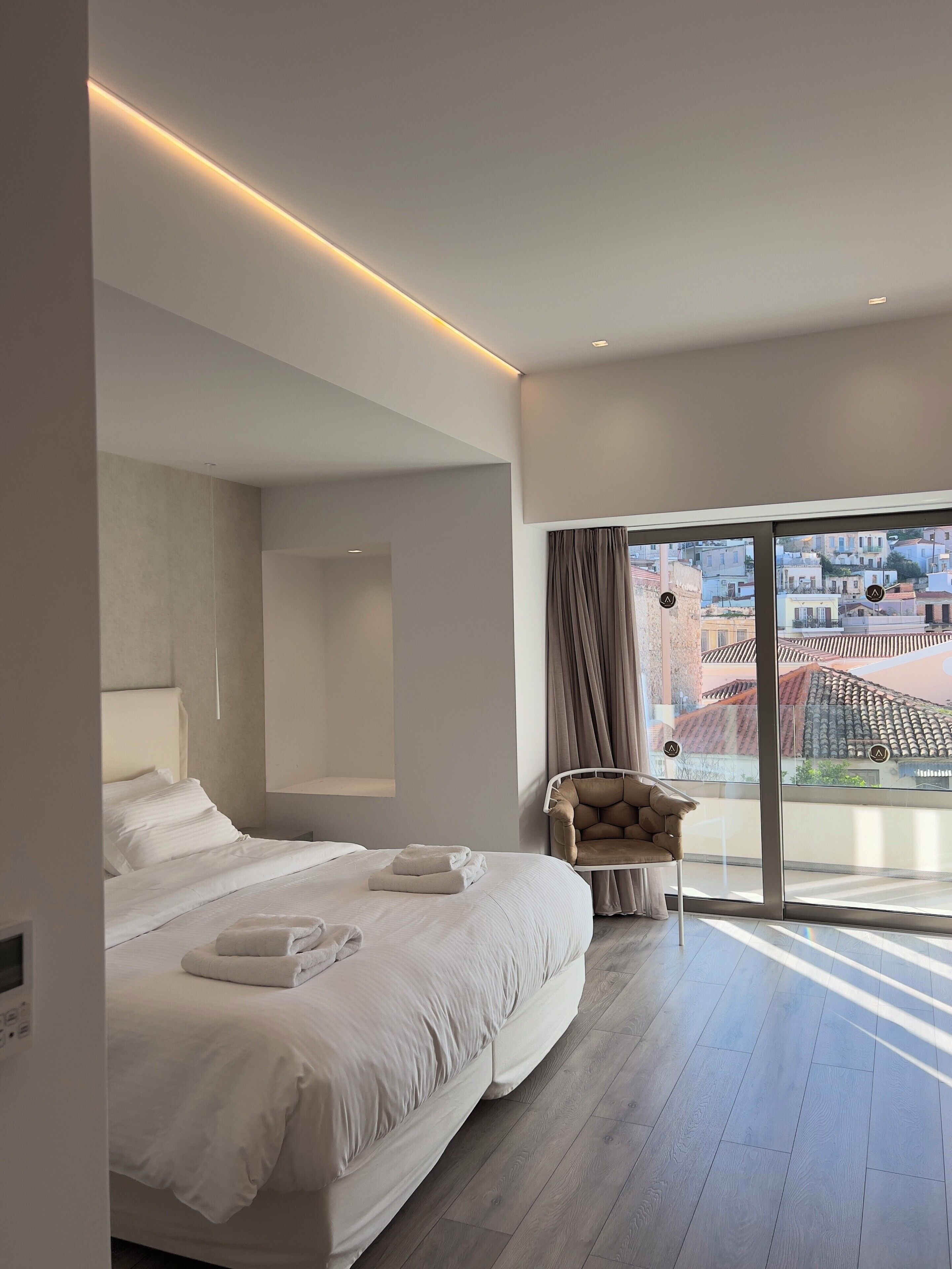 A modern hotel room with a large bed, a chair, and a balcony with a city view.