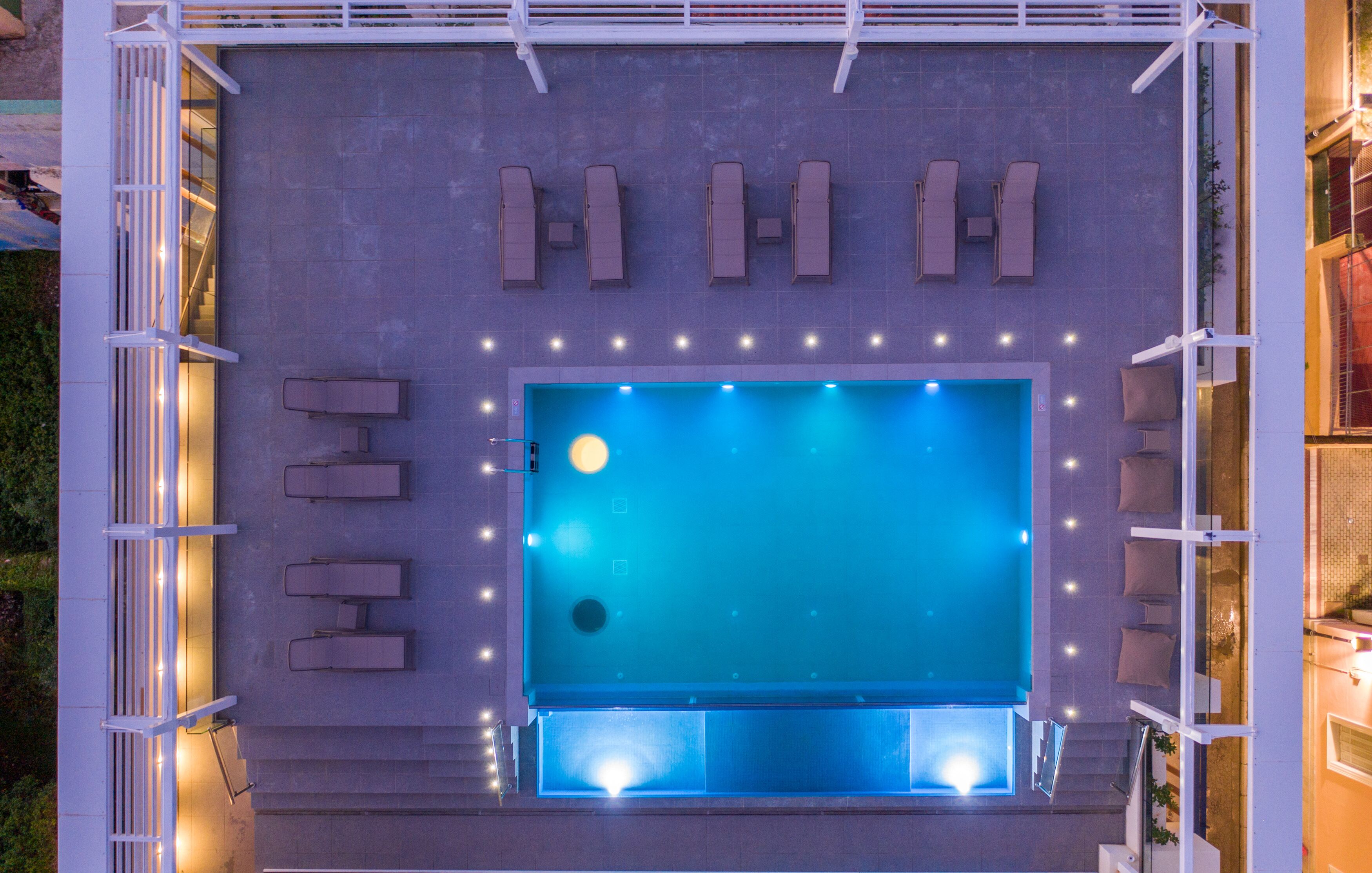 An aerial view of a swimming pool with lounge chairs and lights, surrounded by a white structure.