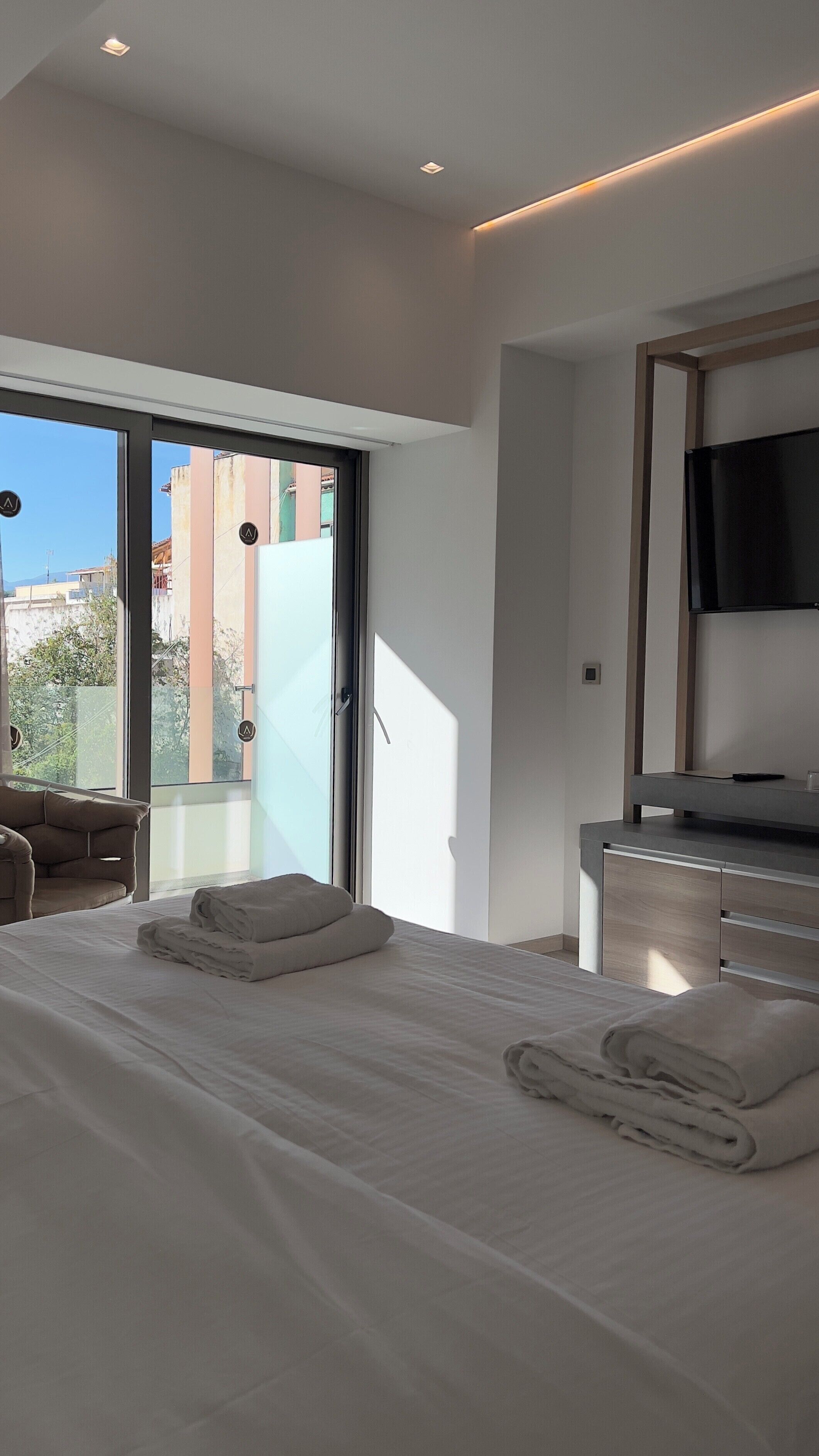 Una habitación de hotel moderna con una cama grande, un televisor de pantalla plana y un ventanal corredero que da a un balcón.