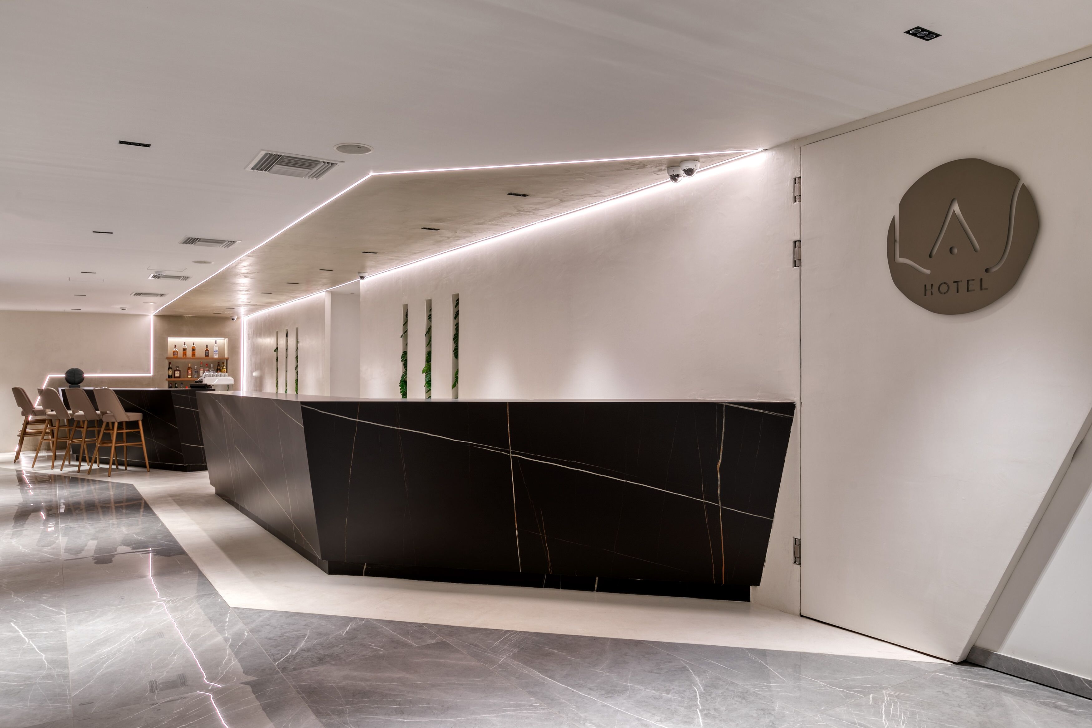 A modern hotel reception area with a sleek black reception desk, a minimalist design, and a visible "HOTEL" sign on the wall.