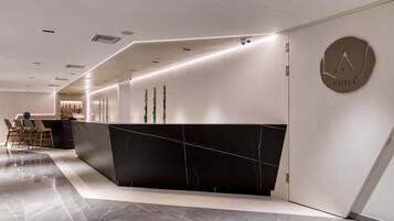 A modern hotel reception area with a sleek black reception desk, a minimalist design, and a visible "HOTEL" sign on the wall.