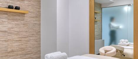 Un moderno spa con pared de madera, un espejo grande y toallas dobladas sobre una mesa de masaje.
