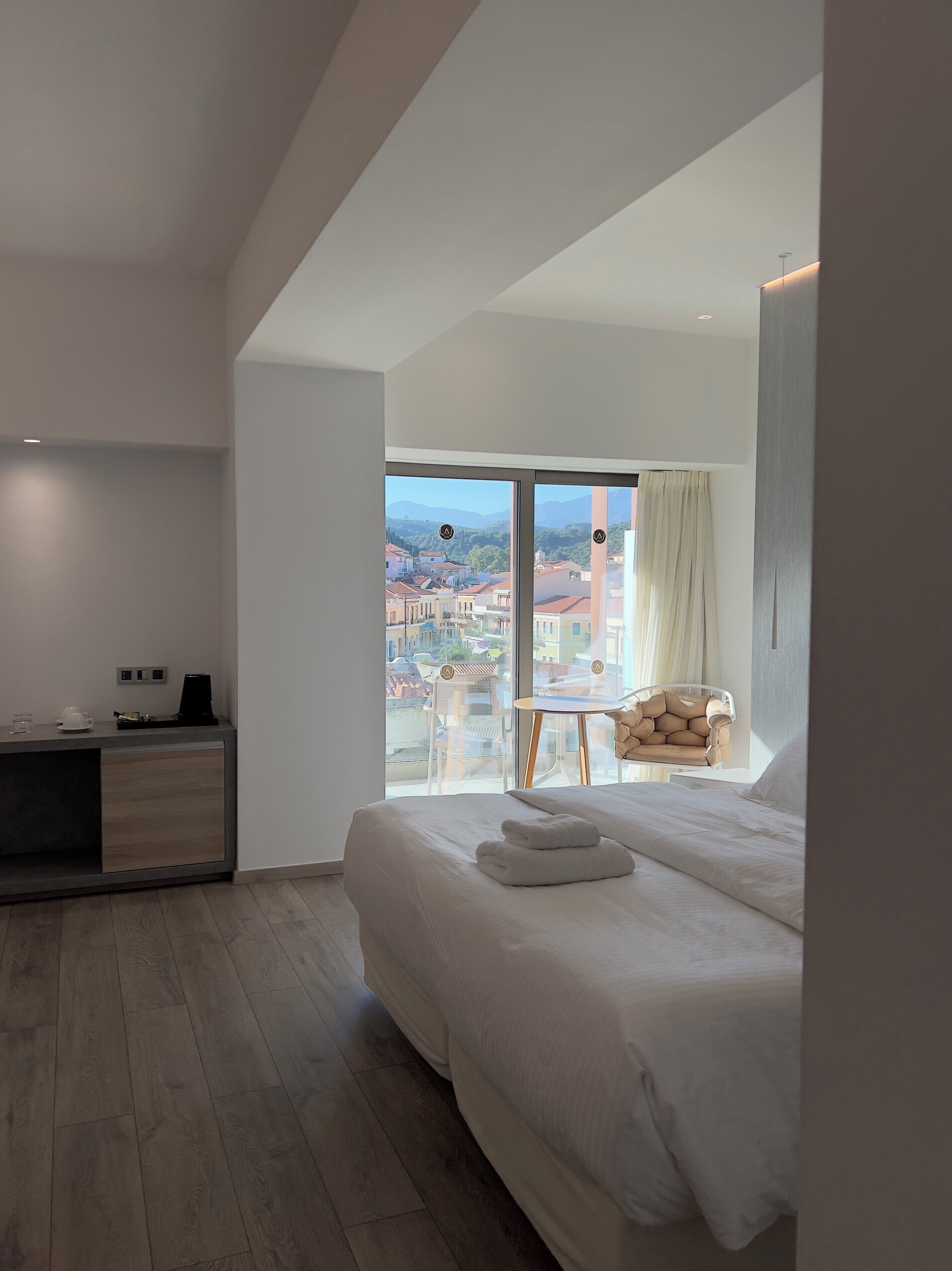 A modern hotel room with a large bed, a desk, a chair, and a balcony with a city view.
