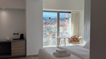 A modern hotel room with a large bed, a desk, a chair, and a balcony with a city view.