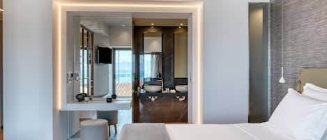 A modern hotel room with a large bed, a desk with a computer, a vanity with a mirror, and a view of the city.