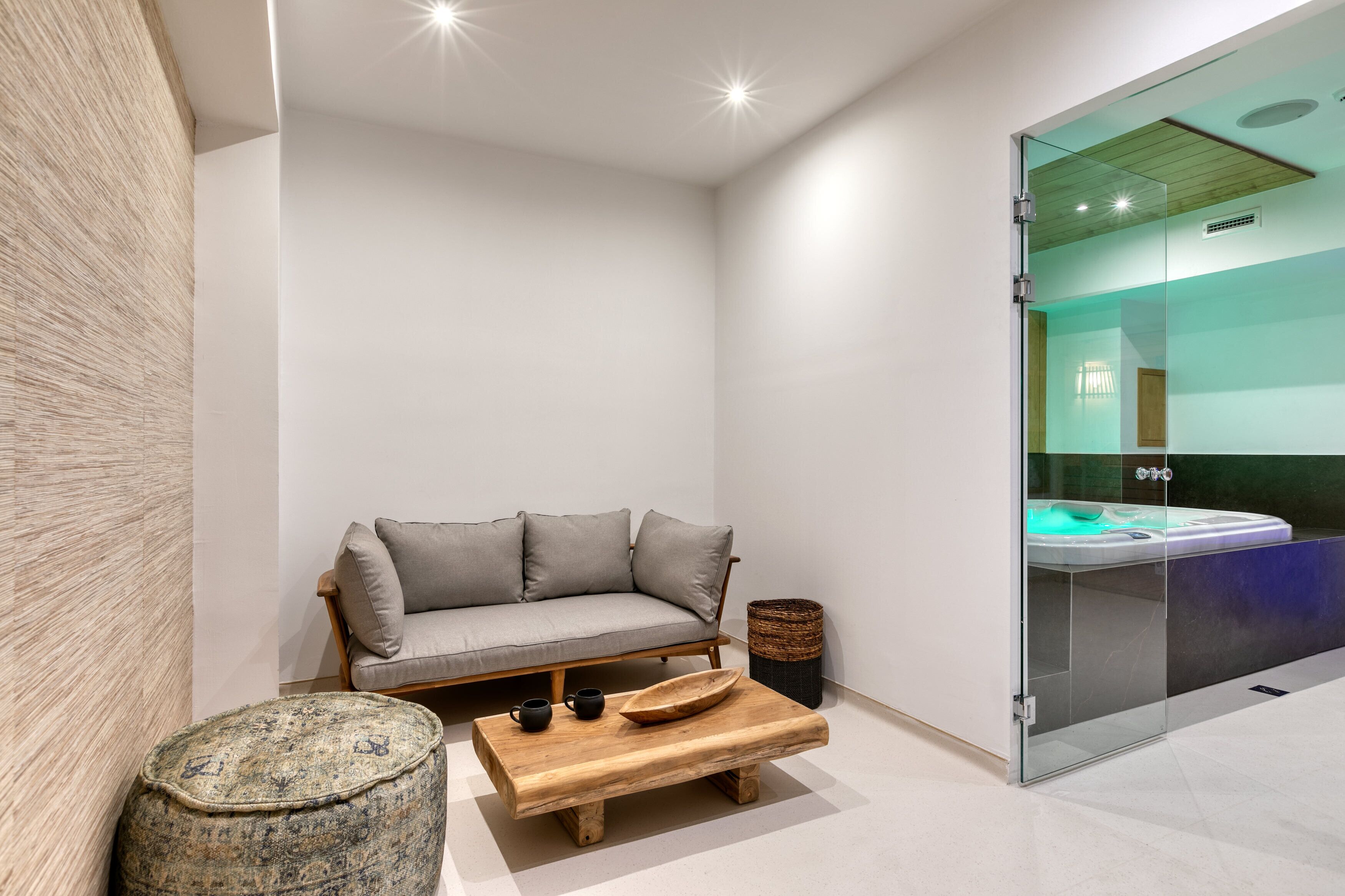 A modern, minimalist bathroom with a glass-enclosed shower, a wooden bench, and a grey sofa.