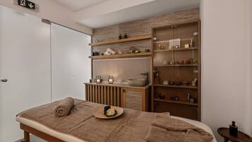 A modern spa room with a massage table, shelves with toiletries, and a wooden vanity.
