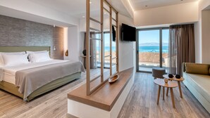 A modern hotel room with a large bed, a seating area with a table, and a view of the sea.