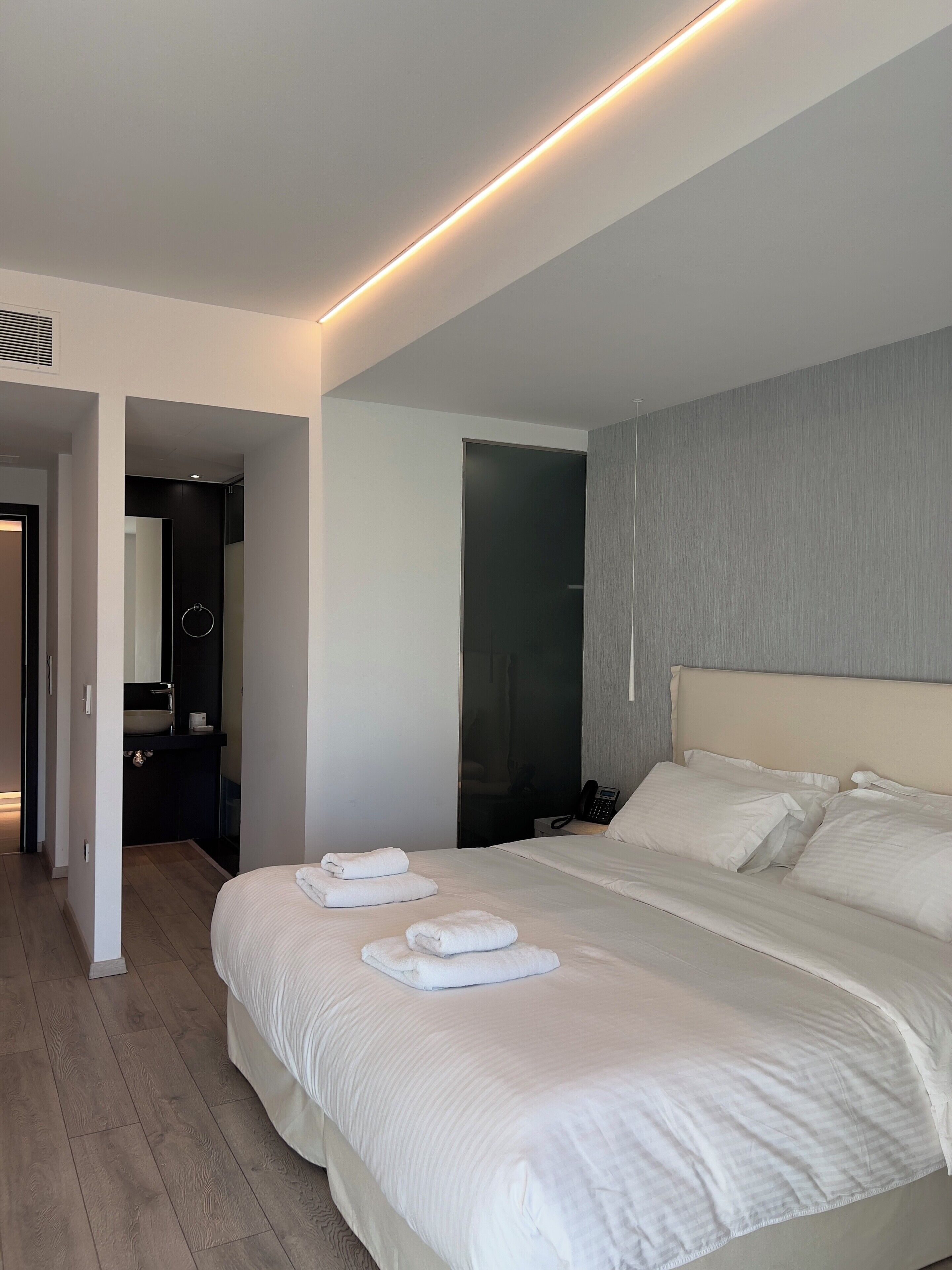 Una camera d'albergo moderna con un letto grande, un telefono sul comodino e un bagno visibile tramite una porta aperta.