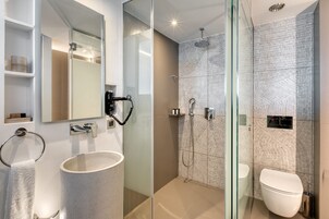 Un baño moderno con ducha de vidrio, lavamanos blanco y un inodoro.
