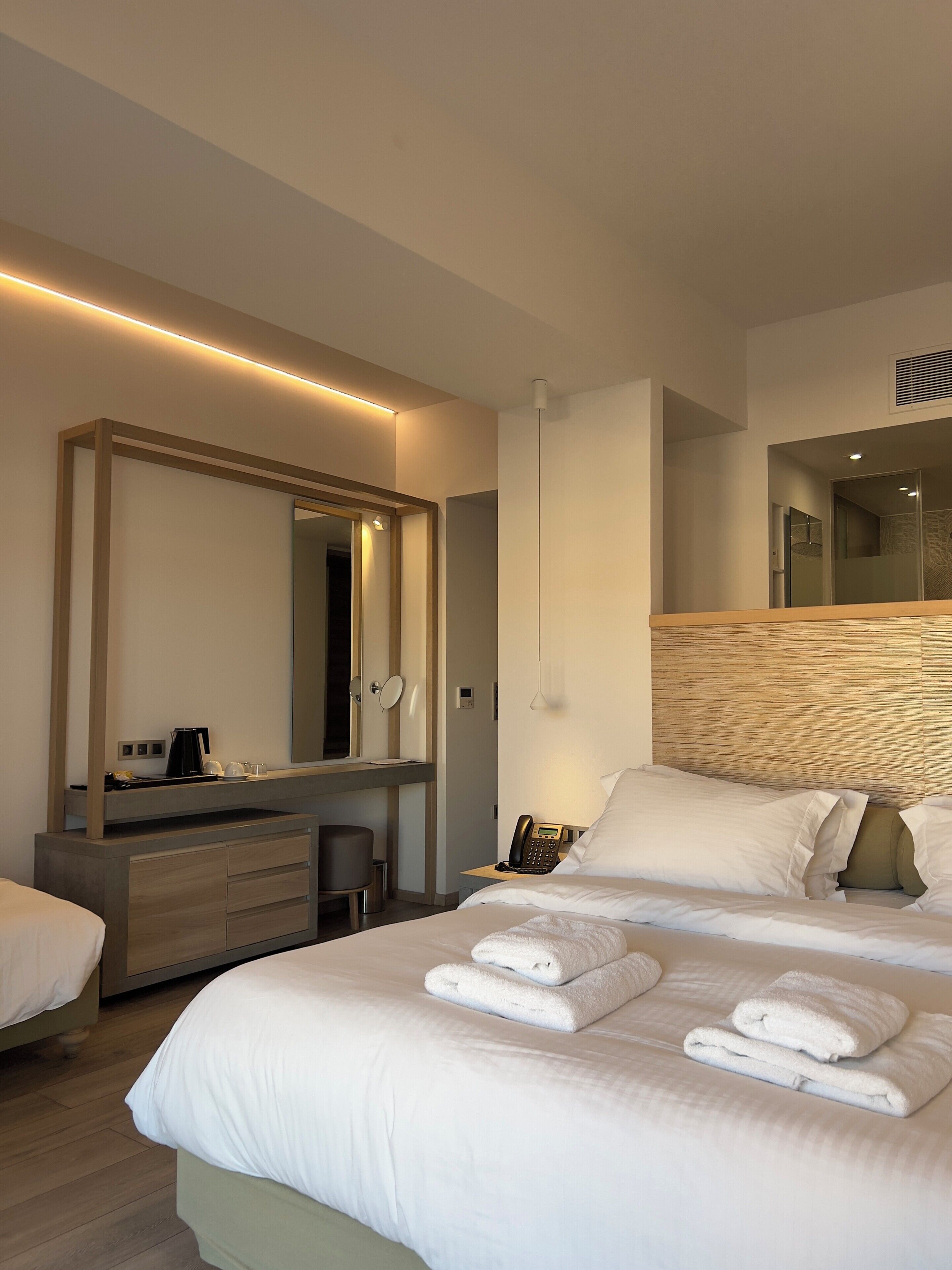 A modern hotel room with a large bed, a bedside table, a mirror, and a desk with a chair.