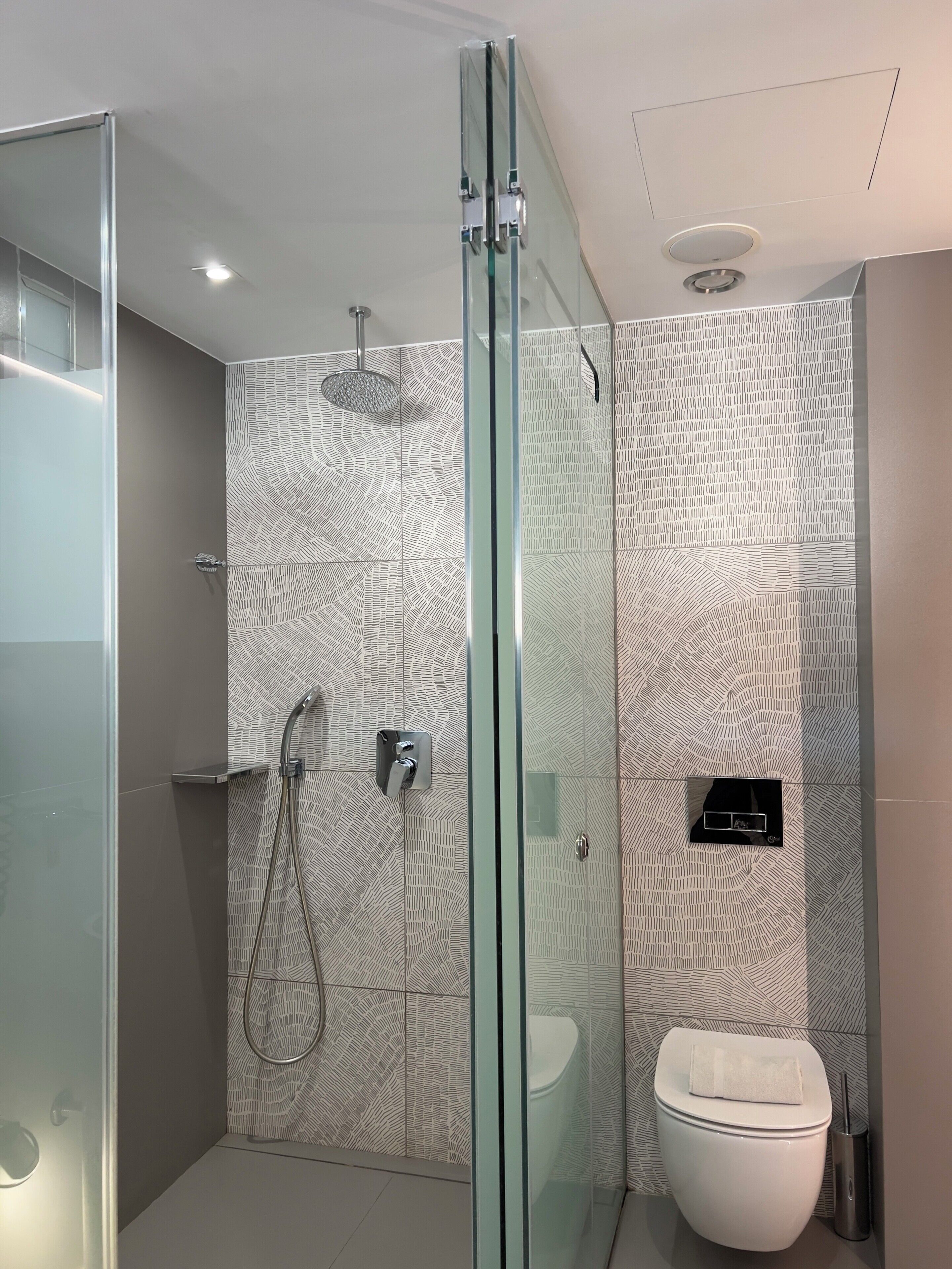 Un baño moderno con cabina de ducha de vidrio, inodoro y pared con diseño.