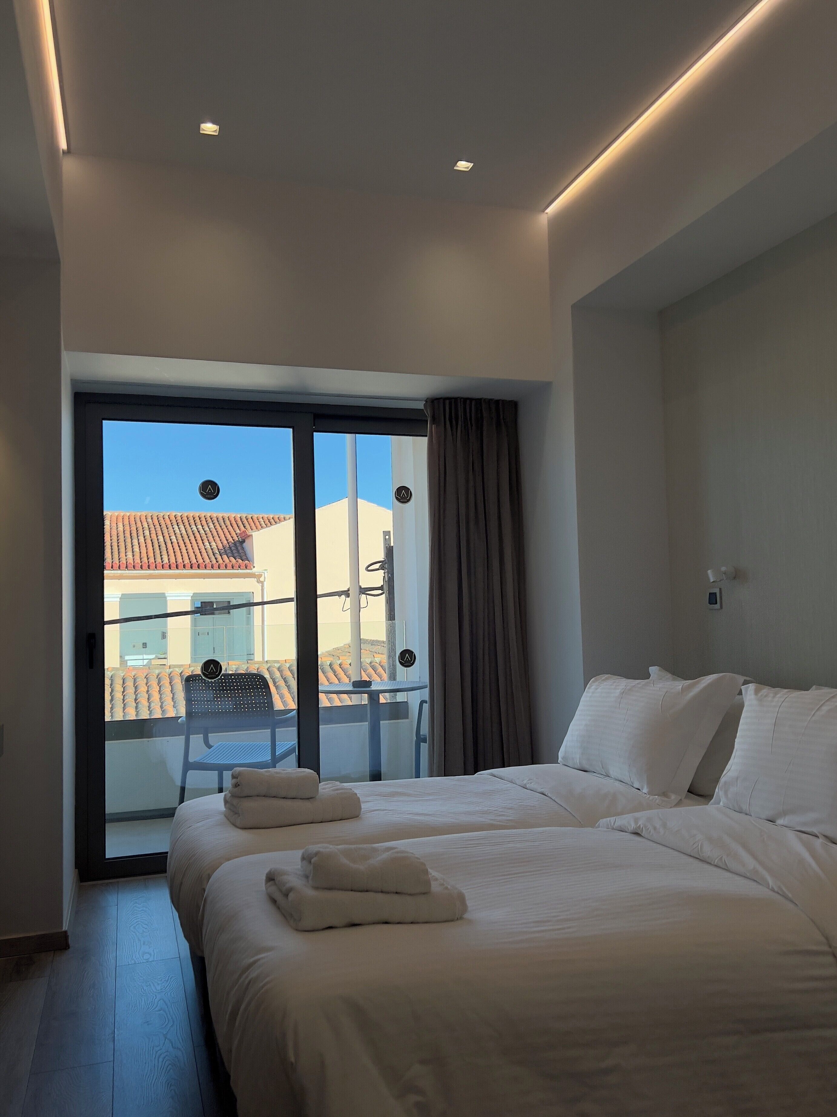 Una habitación de hotel con cama, una silla, un balcón con vistas y una lámpara en el techo.