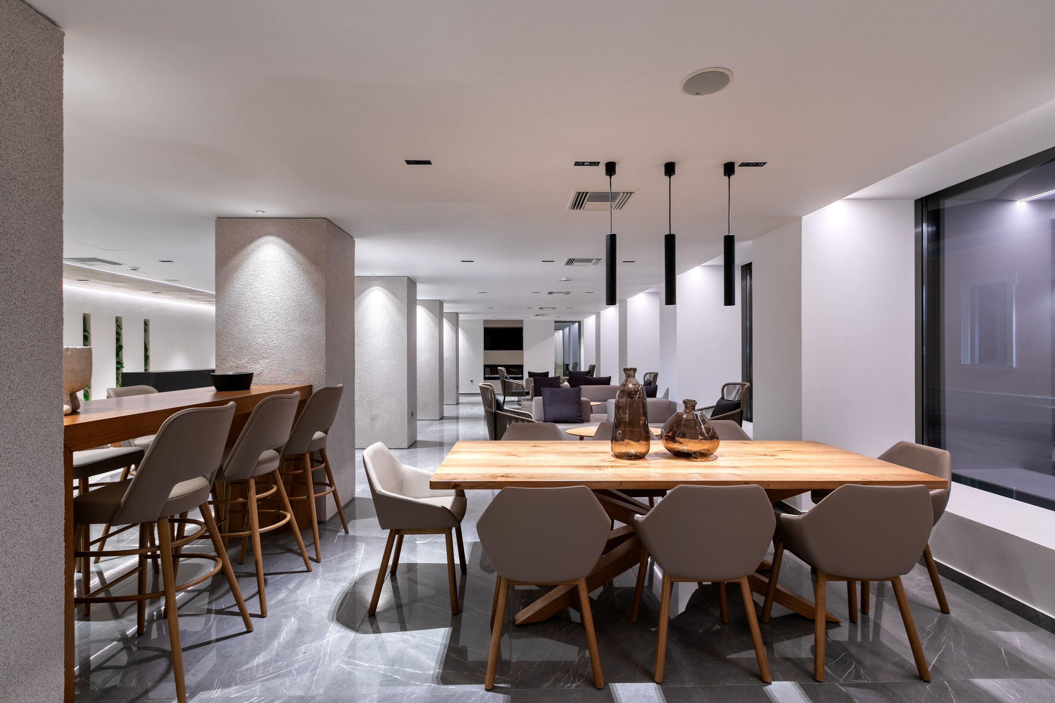 A modern dining area with a wooden table and chairs, pendant lighting, and a view through a glass wall.