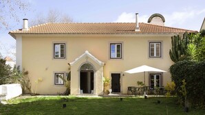 A two-story house with a tiled roof, a central entrance with a decorative arch, and a small patio area with outdoor furniture. - Palácio de Sintra Boutique House (Sintra)