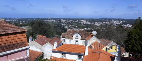 A view of a town with terracotta-roofed buildings, a prominent white building with a balcony, and a clear blue sky.