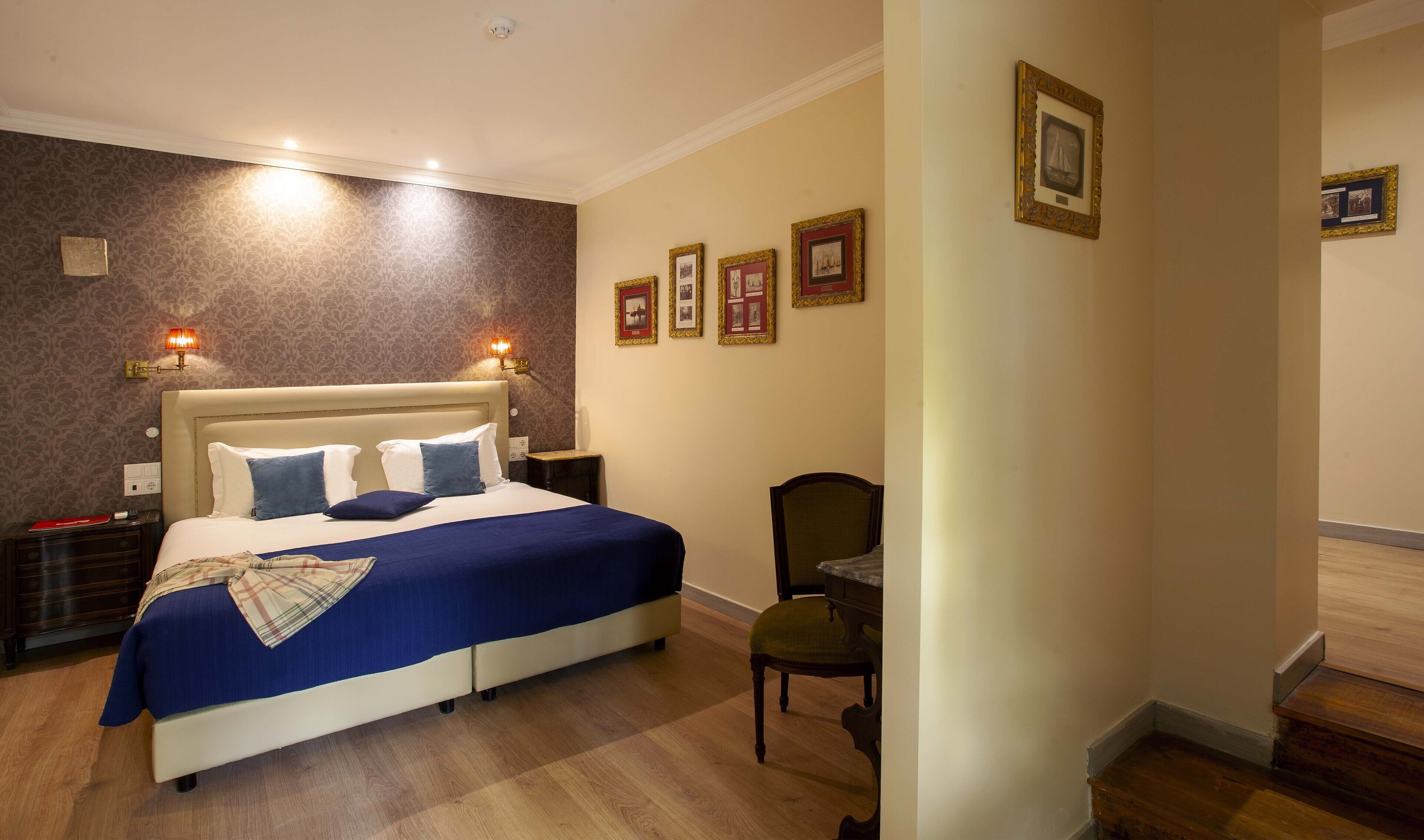 Una habitación de hotel con una cama grande, dos mesitas de noche, una silla y una pared decorada con cuadros.