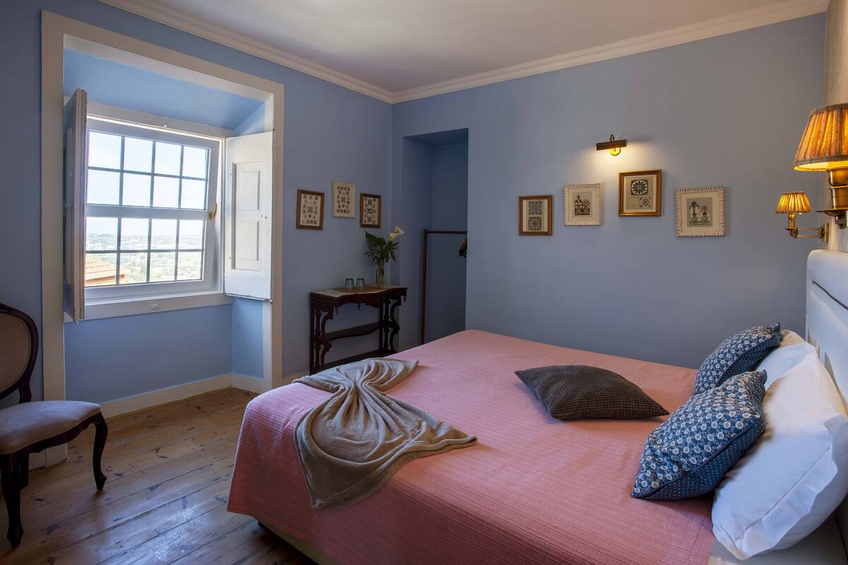 Ein Schlafzimmer mit einem Bett, einem Sessel, einem Schreibtisch und einem Fenster.