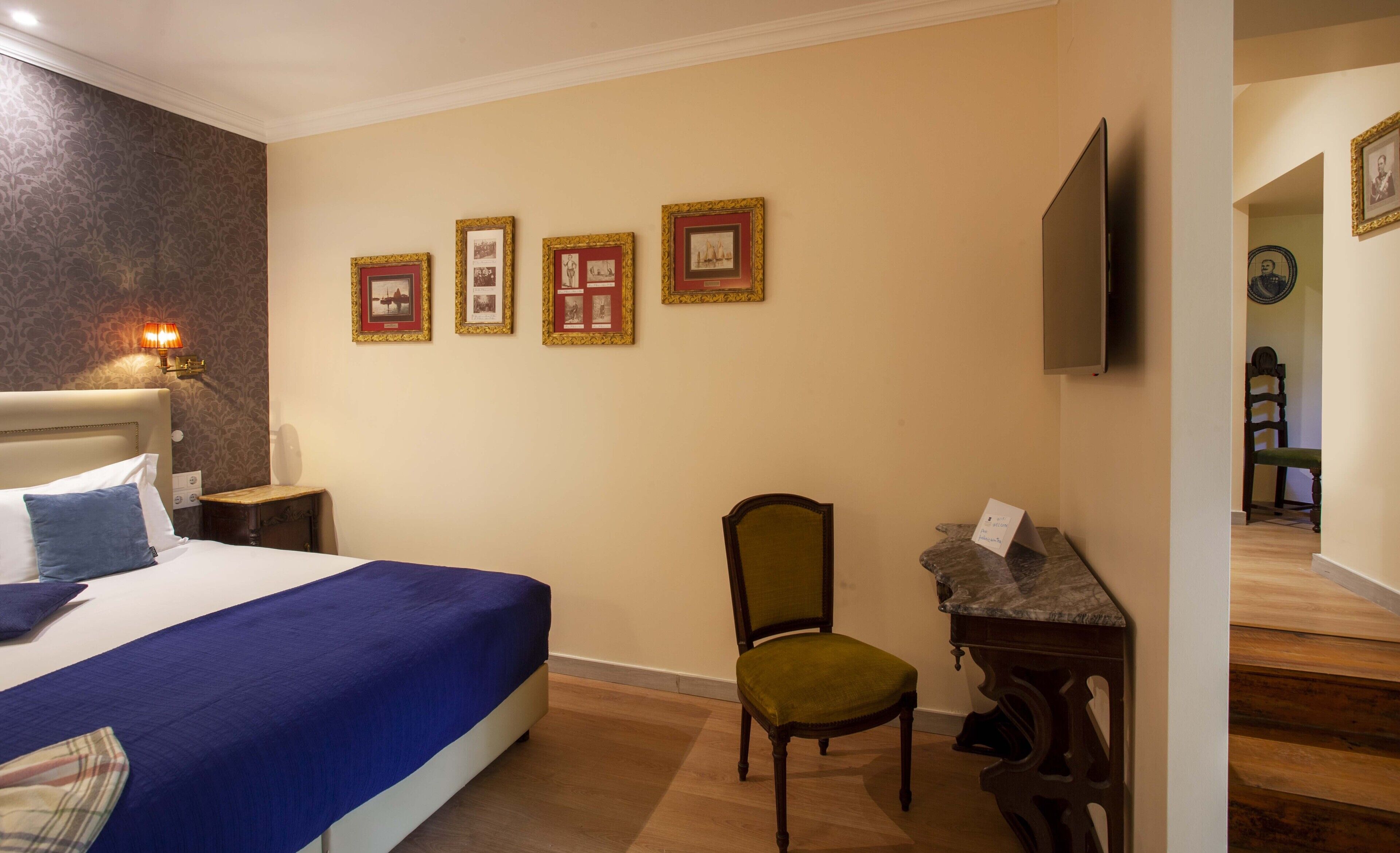 Ein Hotelzimmer mit einem großen Bett, einem Sessel, einem Schreibtisch mit Computer und gerahmten Bildern an der Wand.