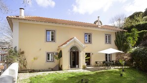 A two-story building with a tiled roof, a central entrance with a cross, and a patio area with outdoor seating. - Palácio de Sintra Boutique House (Sintra)