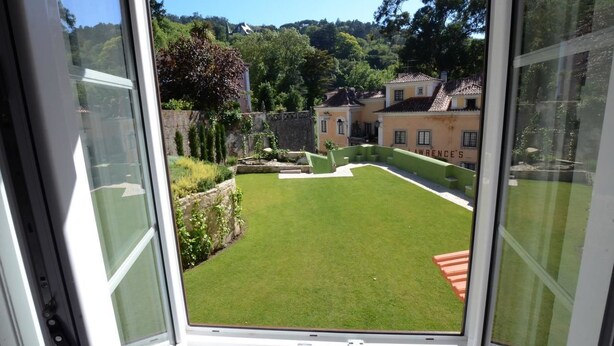 A view through a window of a well-maintained lawn with a stone wall and a building labeled "Warren's" in the background. - Palácio de Sintra Boutique House (Sintra)