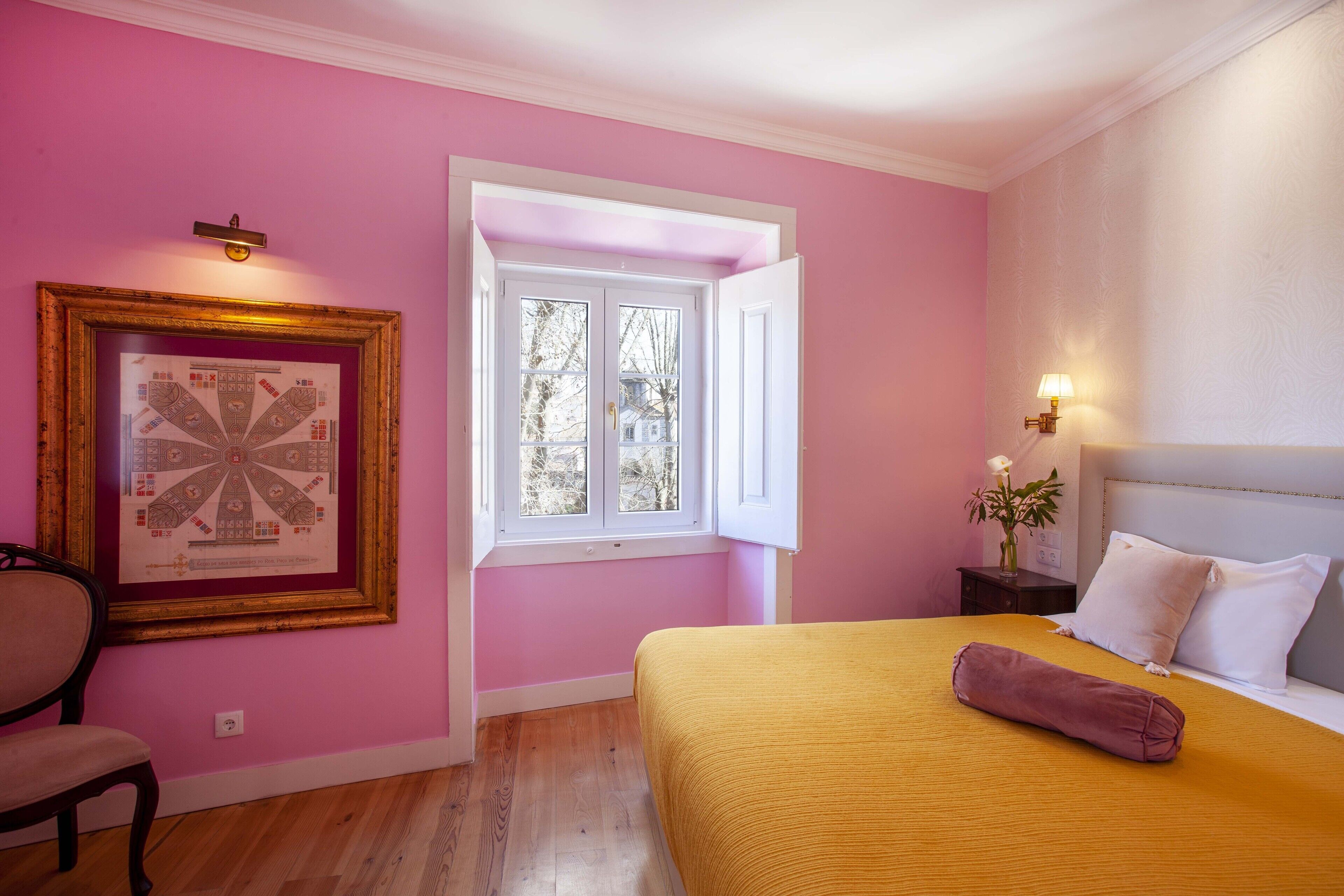 Een slaapkamer met een bed, een raam, een stoel en een lijst met een afbeelding aan de muur.