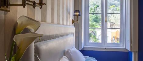 A hotel room with a bed, a nightstand, a lamp, a window with a view, and a plant.