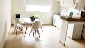 A modern kitchen with white cabinets, a granite countertop, and a dining area with a white table and chairs. - Buda Apartments (San Rafael)