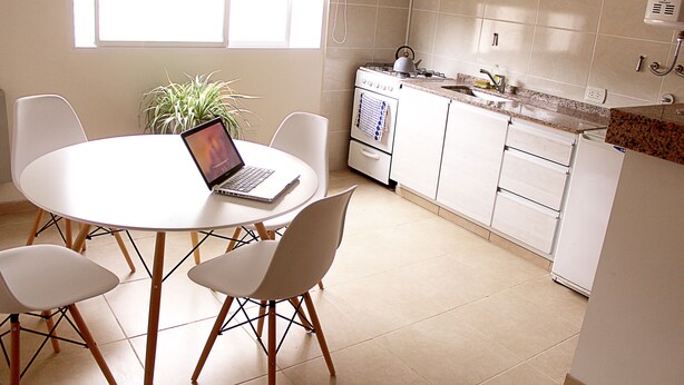A modern kitchen with white cabinets, a stove, and a dining table with chairs. - Buda Apartments (San Rafael)