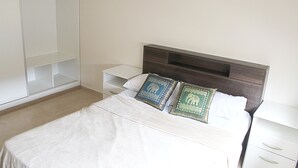 A neatly made bed with two decorative pillows, a bedside table, and a wardrobe in a hotel room. - Buda Apartments (San Rafael)