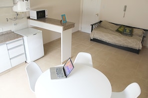 A compact room with a kitchenette, a bed with decorative pillows, a laptop on a table, and a white chair. - Buda Apartments (San Rafael)