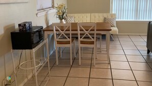 Ruokailutila, jossa on pöytä ja tuolit, mikroaaltouuni jalustalla, maljakko ja taulu seinällä.