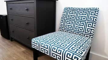 Een stoel met een geometrisch patroon bekleding en een donkere houten dressoir met drie laden.
