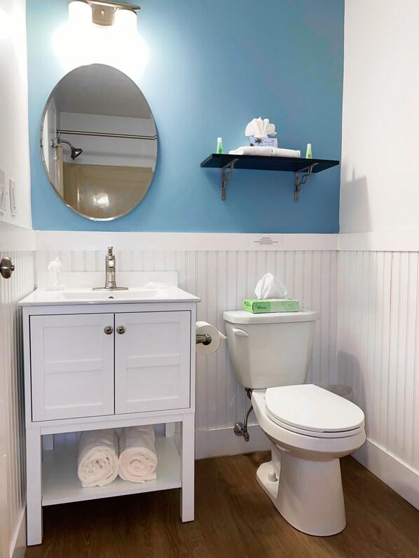 Une salle de bain avec un meuble-lavabo blanc, un miroir rond, des toilettes et une étagère contenant des articles de toilette.