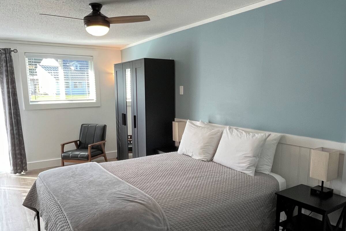 A bedroom with a bed, a nightstand, a chair, a wardrobe, and a ceiling fan.