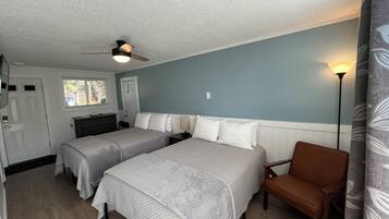 A bedroom with two beds, a chair, a desk, and a ceiling fan.