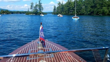 Un bateau arborant un drapeau, entouré d’une eau calme et de quelques arbres à l’horizon.