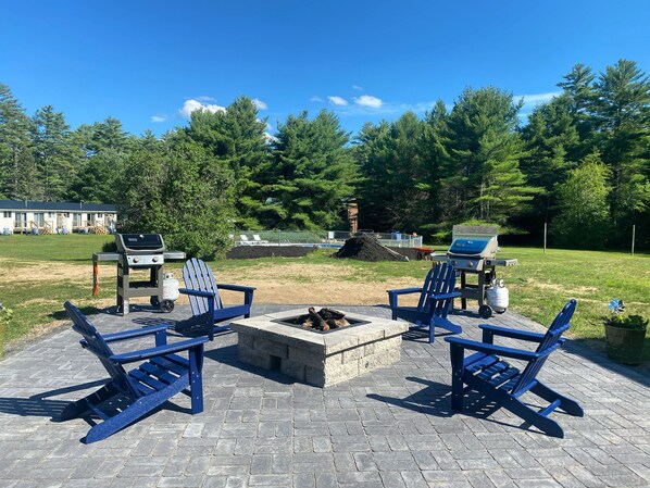 A patio with Adirondack chairs, a fire pit, and barbecue grills.