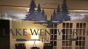 Een receptiegedeelte met een bord voor Lake Wennington Inn, waarop een berg en meer silhouet afgebeeld is. Er staan twee leren stoelen en een bijzettafeltje met een lamp.