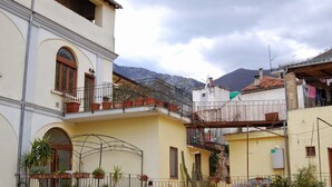 Un edificio de varios pisos con balcones, plantas en macetas y montañas al fondo.